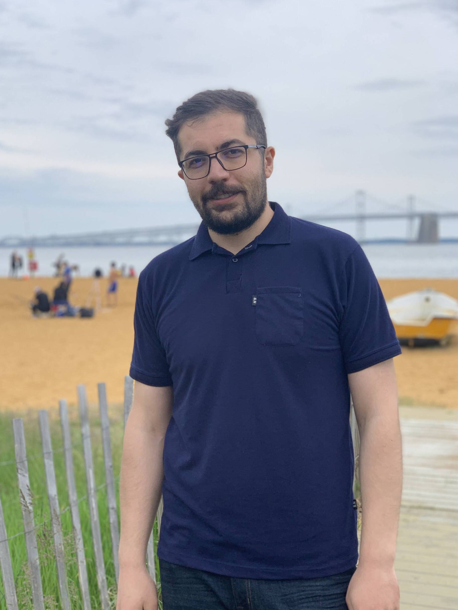 Jamshid Jalali poses for a photo with a beach and suspension bridge in the background.